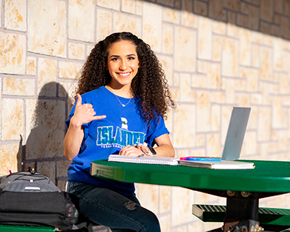student Claudia Narvaez sitting with her lap top outside on campus